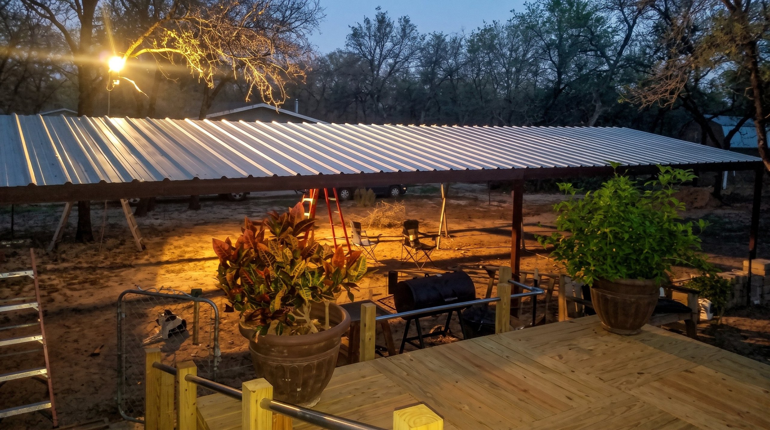 Large steel carport cover next to a wooden deck at dusk in Texas