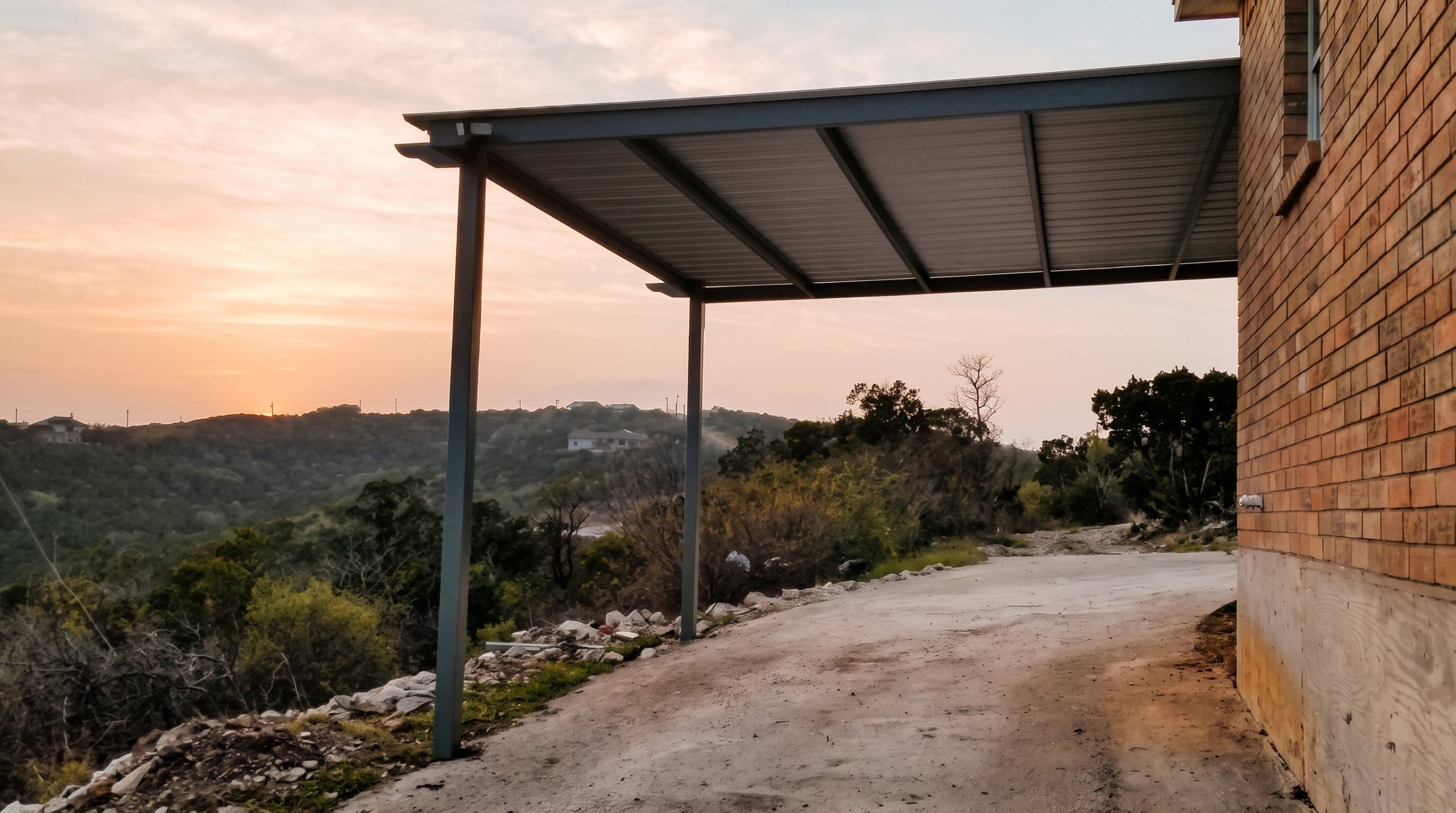Steel carport attached to a brick house in the Texas Hill Country at sunset
